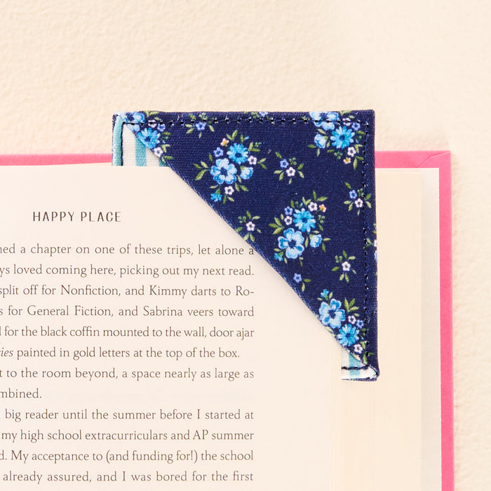 A close-up of an open book corner with the-darling-effect’s Endless Daydream Navy Corner Keeper Fabric Bookmark slipped over the top right edge—a perfect gift for any book lover.