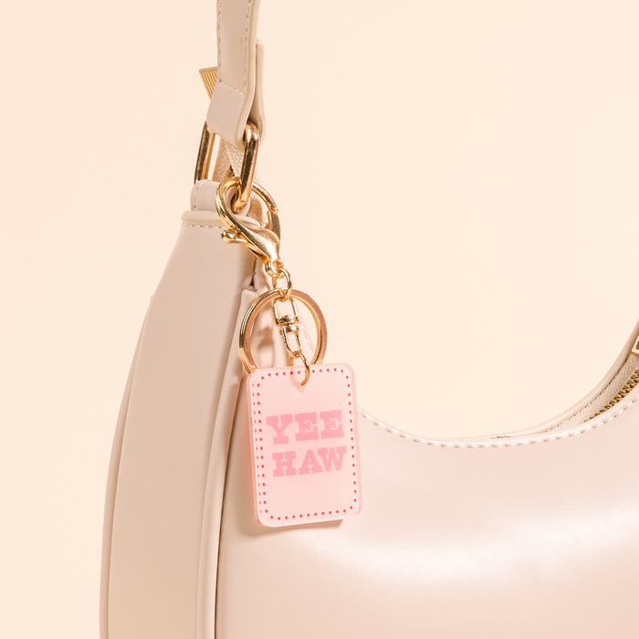 A close-up of the-darling-effect’s Yeehaw Acrylic Keychain in pink, attached to a light beige handbag—perfect for anyone who loves cute accessories.