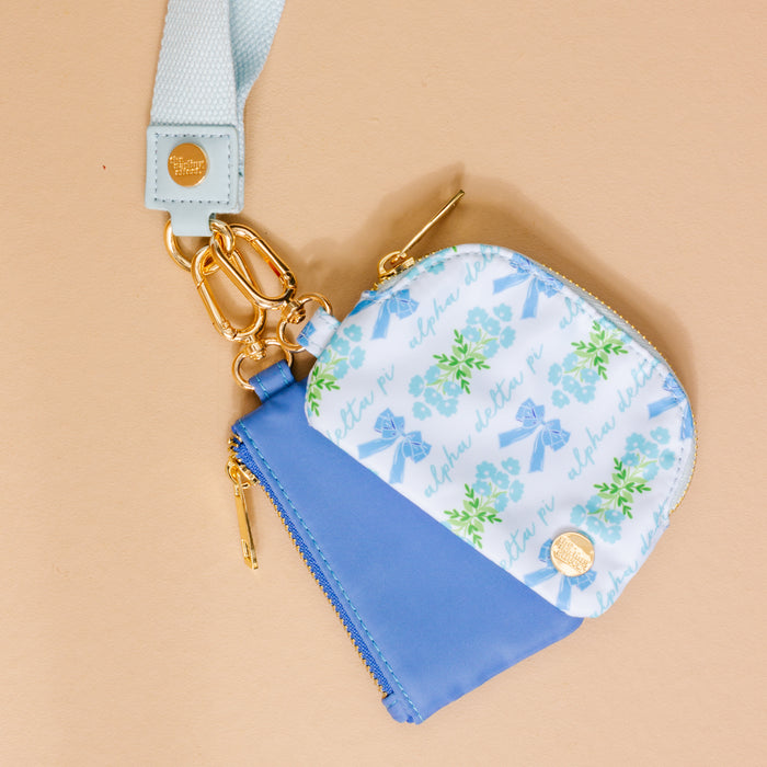 The Darling Effect Alpha Delta Pi Dynamic Duo Pouch Wristlet features two small zippered pouches, including a blue floral ADPi design, clipped together with gold hardware and a light blue wristlet strap with gold emblem.