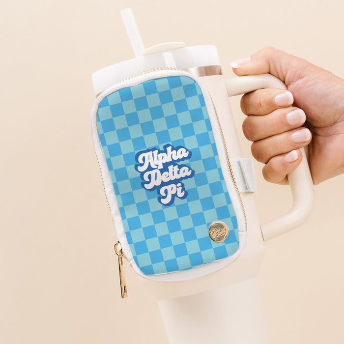 A hand holds The Darling Effect's Alpha Delta Pi Tumbler Fanny Pack—a white tumbler with a built-in straw and a blue checkered, water-resistant fanny pack attached, featuring "Alpha Delta Pi" in white script.