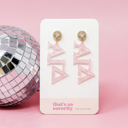 The Darling Effect’s Alpha Gamma Delta Letter Pink Acrylic Earrings hang on a “that’s so sorority collection” card, set against a pink background with a silver disco ball on the left—perfect for a bid-day basket.