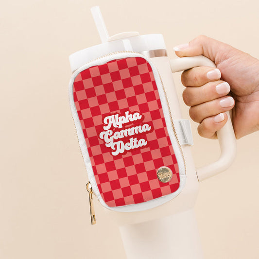 A hand holds a large white tumbler with a handle, featuring The Darling Effect's Alpha Gamma Delta Tumbler Fanny Pack—a water-resistant pouch in red and pink checkered pattern with “Alpha Gamma Delta” in white script on the front.