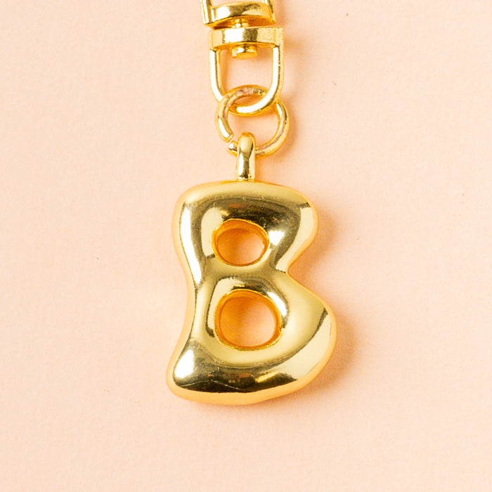 The-darling-effect B Bubble Letter Keychain Bag Charm features a shiny gold bubble letter B on a rose gold chain, perfect for adding a personalized touch to your keys or bag.