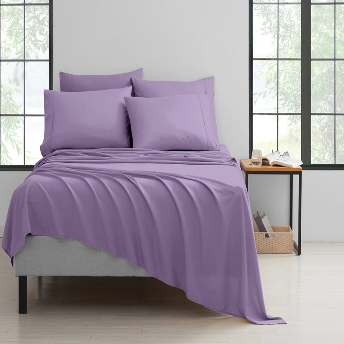 Purple bedding set on a bed in a room with large windows.