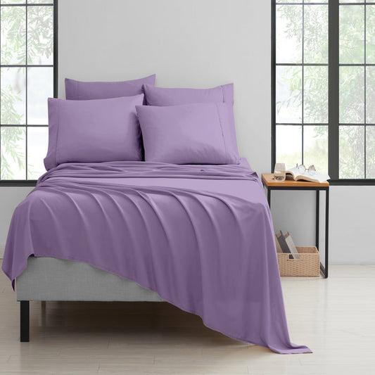 Purple bedding set on a bed in a room with large windows.