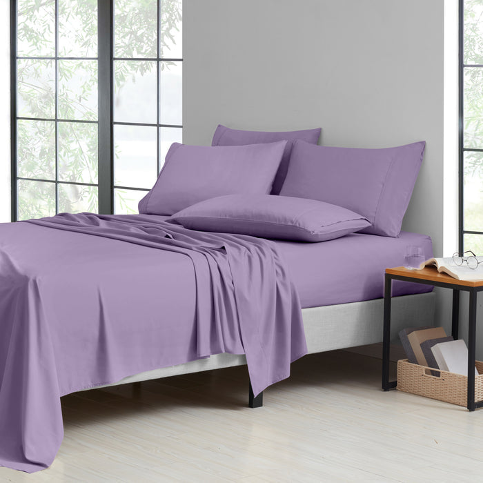 Purple bedding set on a bed in a room with large windows.
