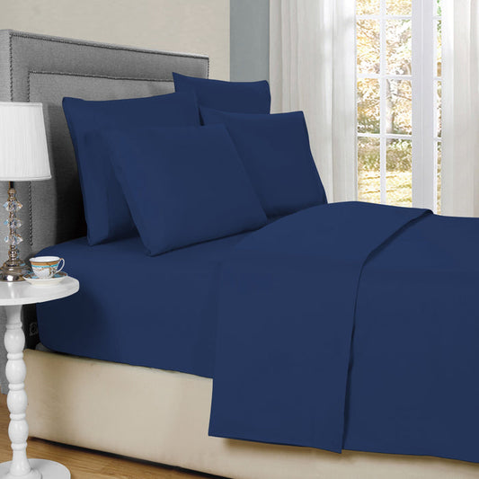 Navy blue bed sheets and pillows on a neatly made bed with a side table and lamp in the background.