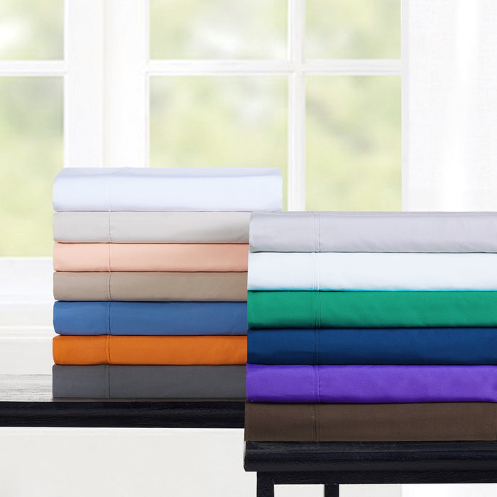 Stack of folded bed sheets in various colors on a table with a window in the background.
