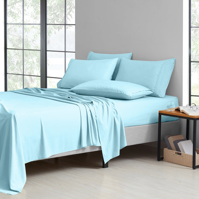 Light blue bedding set on a bed in a room with large windows.