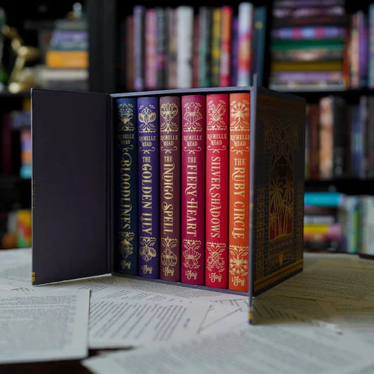 Bloodlines Special Edition Box Set by Richelle Mead – open hardcover box set displaying six gold-foiled book spines on a desk with manuscript pages in the background