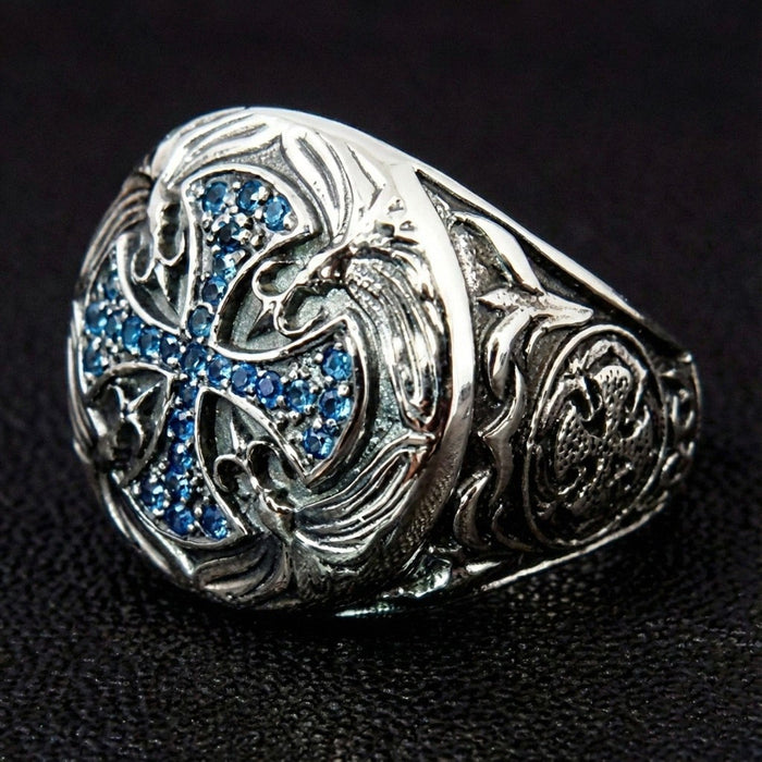 Left angle showing raised floral carvings and blue CZ cross detail on oxidized sterling silver