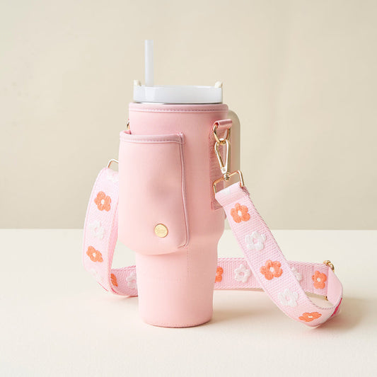 The Darling Effect Blush Tumbler Sling holds a pink handled tumbler with straw in a neoprene bag featuring a pocket, gold snap closure, adjustable strap, and orange and white floral pattern.