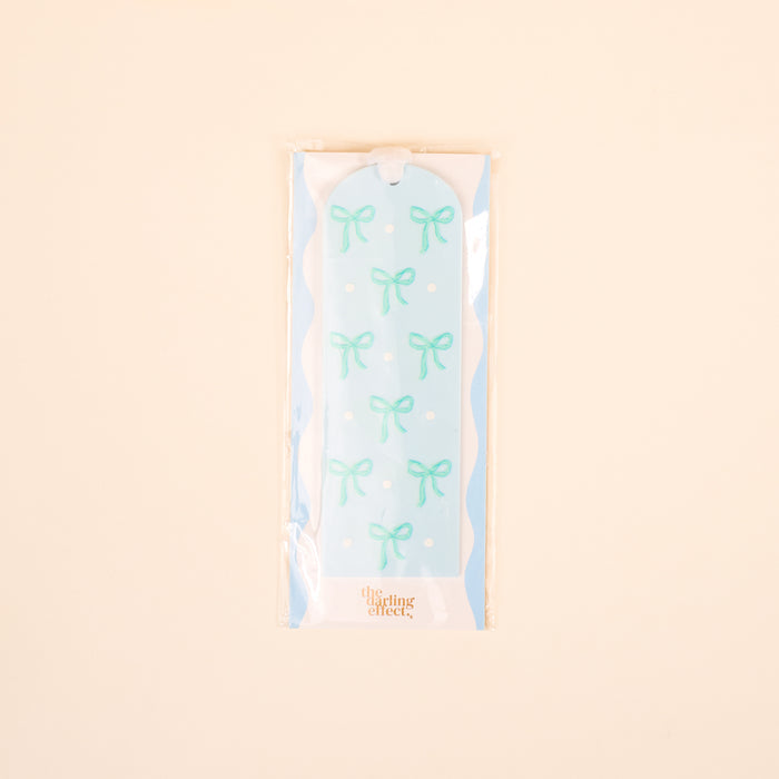 The Bows Blue Acrylic Bookmark by the-darling-effect features a light blue design with light green bows and white polka dots. Packaged in plastic, it's a charming gift for book lovers.