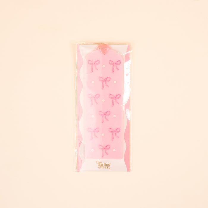 The-darling-effect’s Bows Pink Acrylic Bookmark features pink bows and white dots, packaged in clear plastic with a cream background—a delightful gift for book lovers and collectors of cute bookmarks.