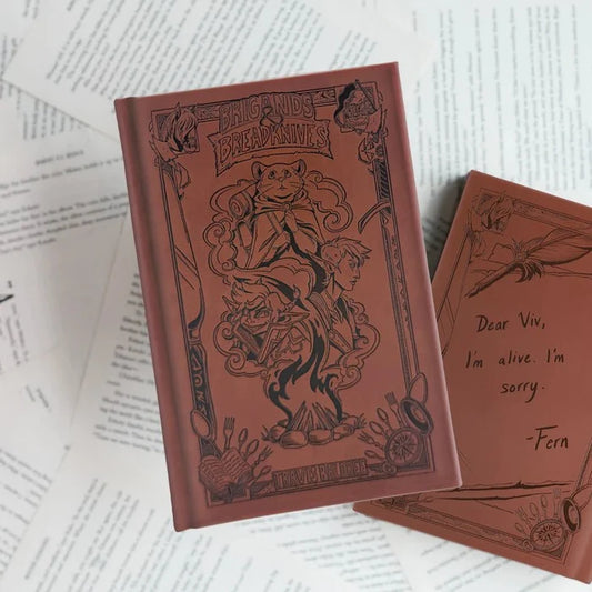 Brigands & Breadknives LitJoy Edition hardcover with debossed gothic-style cover art, shown atop open book pages with a handwritten note