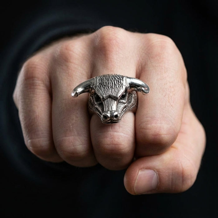 Silver bull head ring with textured horns and detailed facial features displayed on a clenched fist against a dark background