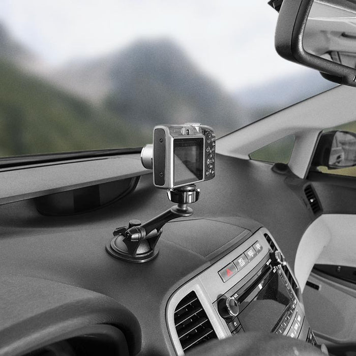 A Camera Holder with Sticky Suction Mount and Adhesive Disk is attached to a car dashboard, securing a camera aimed at the windshield with blurred mountains visible in the background.