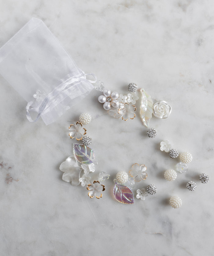 The Candyman Pearl Kit by WALD Berlin is a sheer white drawstring bag featuring pearly beads and floral details, artfully displayed on a marble surface.