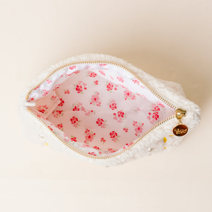 The Darling Effect's Chi Omega Bows & Pearls Teddy Pouch features white sherpa, a pink floral lining, gold zipper, and embroidered bows—making it an adorable gift for any sorority member.