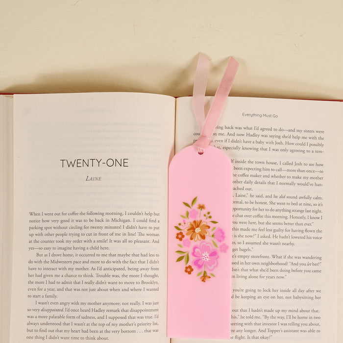 An open book lies flat with the Dainty Floral Pink Acrylic Bookmark—featuring floral designs and two pink ribbons—resting on its pages, making a charming gift for book lovers. The visible chapter is titled TWENTY-ONE.