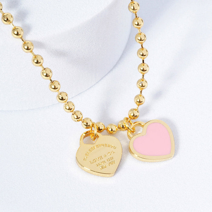 A gold-colored necklace featuring a ball chain design with two heart-shaped pendants.