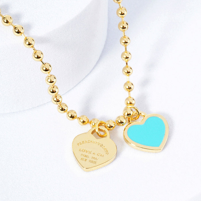 A gold-colored necklace featuring a ball chain design with two heart-shaped pendants.