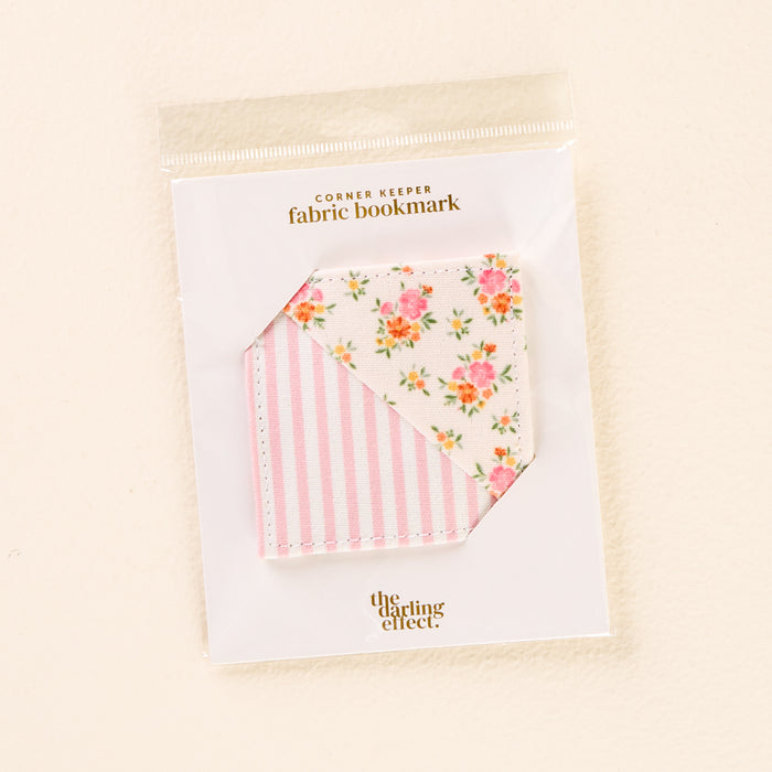 The Endless Daydream Cream Corner Keeper Fabric Bookmark by the-darling-effect features pink stripes and a floral pattern, packaged in a clear sleeve with a "CORNER KEEPER fabric bookmark" label—an ideal gift for book lovers.