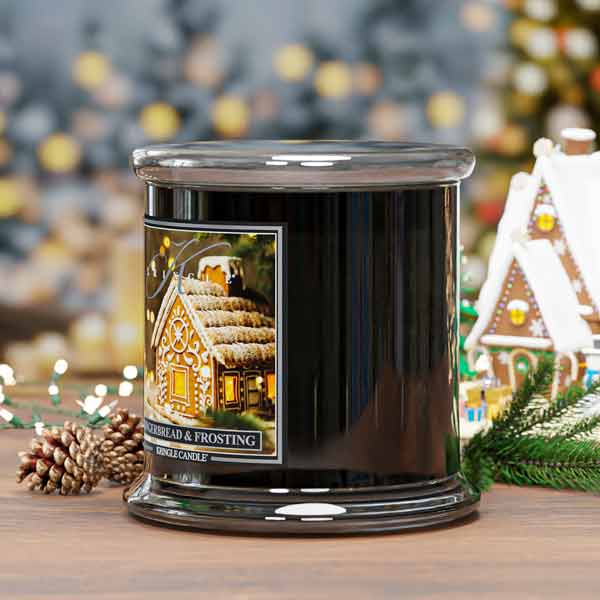Black candle with a gingerbread house design on a wooden surface with festive decorations.