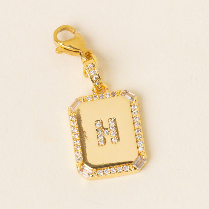 The-darling-effect’s H Jewelry Charm Initial Letter Gold features a gold-plated rectangular pendant with clear gemstones, personalized with an “H” and finished with a lobster clasp—ideal for fans of personalized jewelry.