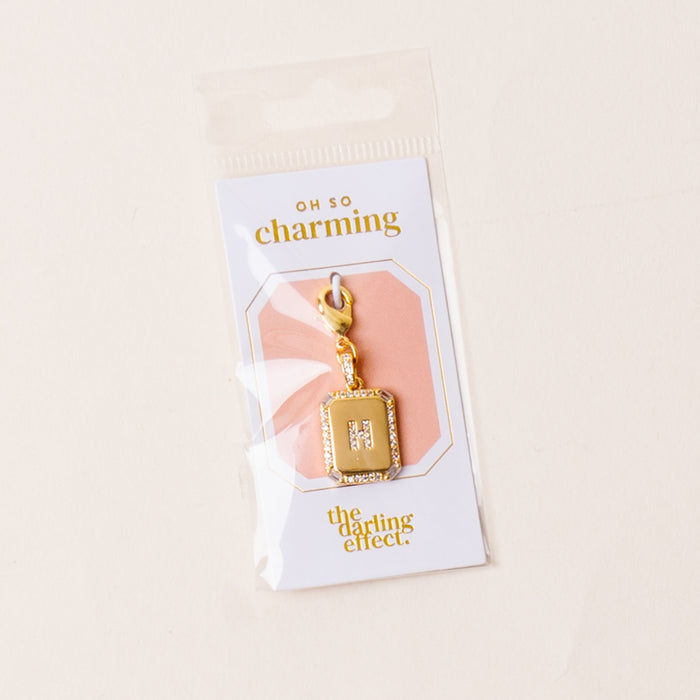The H Jewelry Charm Initial Letter Gold by the-darling-effect features a gold-plated rectangular charm with gem accents, packaged on a white and peach OH SO charming card—ideal for personalized jewelry lovers and sealed in clear plastic.