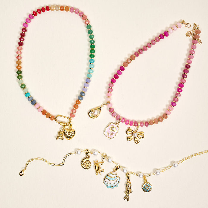 Three vibrant beaded necklaces from the-darling-effect, featuring H Jewelry Charm Initial Letter Gold and playful enamel accents like hearts and cupcakes, are displayed on a light beige background.
