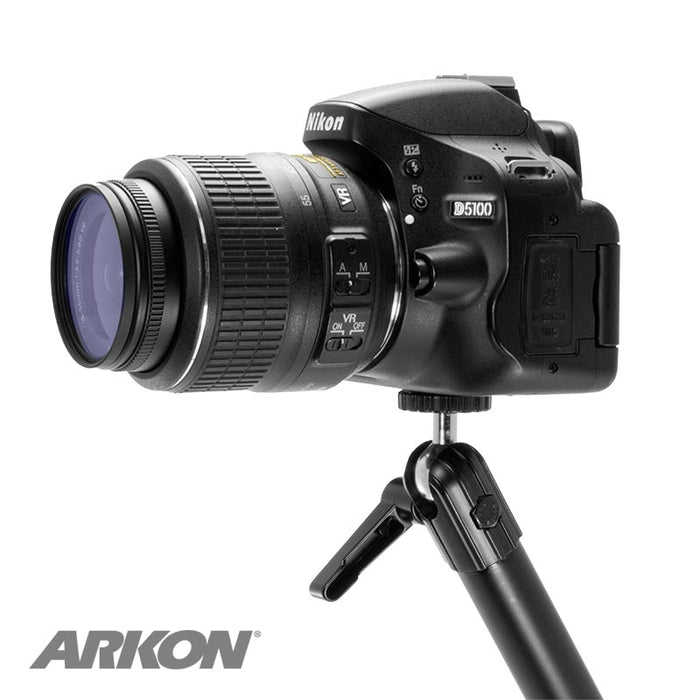 A Heavy-Duty Drill-Base Camera Mount with a 22 adjustable arm holds a Nikon D5100 DSLR camera with zoom lens on a small tripod, set against a white background. The Arkon logo appears in the lower left corner.