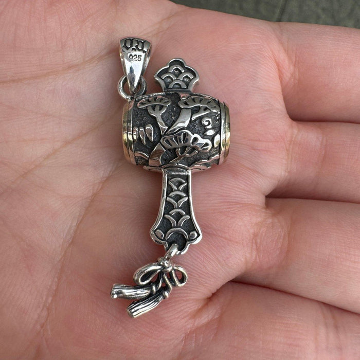 Detailed silver mallet pendant resting in a hand, showcasing the raised pine foliage, 925 bail, and oxidized finish.