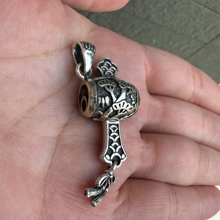 Angled close-up in a palm revealing the deeply carved pine bark handle, raised leaves, and dangling silver tassel.