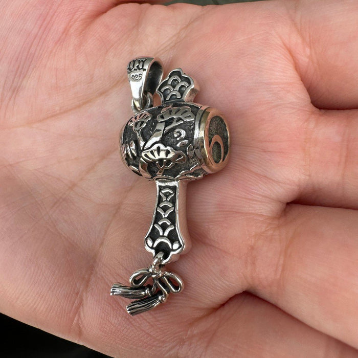Held in an open palm, the oxidized silver gavel pendant displays its raised pine foliage, patterned handle, and 925 bail.