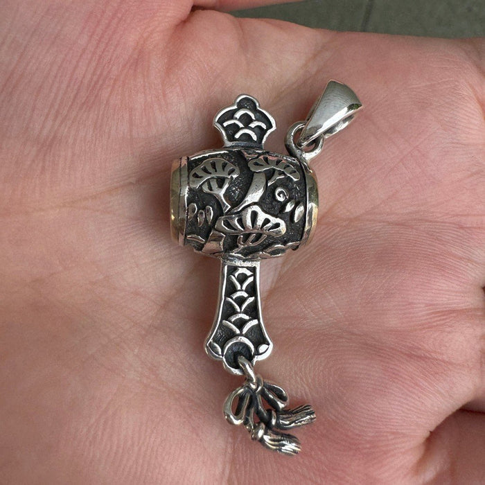 Viewed straight on in a hand, the complete silver mallet charm displays its dark oxidized recesses and raised pine motifs.