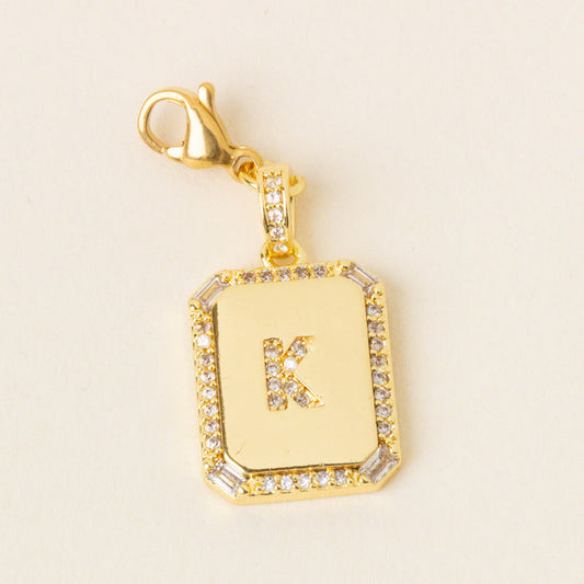 The K Jewelry Charm Initial Letter Gold by the-darling-effect features a rectangular, gold-plated design with diamond and baguette-cut accents on a cream background—ideal for fans of personalized initial letter jewelry charms.