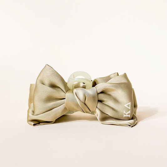 The Darling Effect Kappa Delta Satin Bow Claw Clip is a pale gold satin hair accessory with a clear claw and white KA initials on one tail—ideal for updos or adding elegant charm to any look.