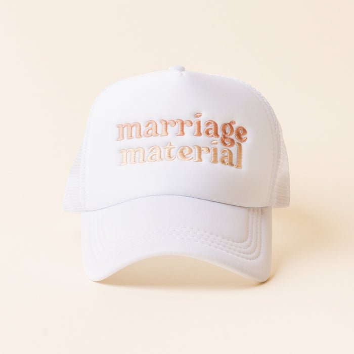The Marriage Material Trucker Hat by the-darling-effect features rose gold embroidered lettering and a trendy "marriage material" phrase on a classic white trucker cap.