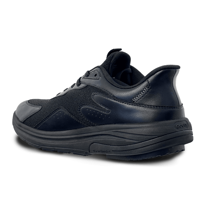 Black athletic shoe with mesh and leather-like upper, thick black sole, shown from a back-angle.