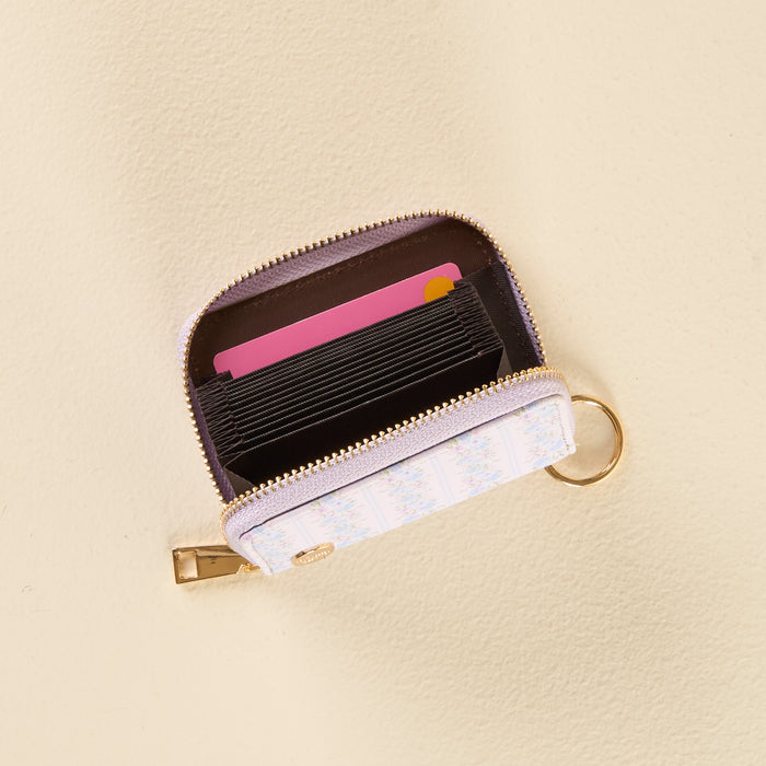 The Petal Parade Blue Zip Around Wallet by the-darling-effect is a small, compact, and stylish accessory featuring a floral pattern, gold zipper, and keyring. Shown open on a beige surface, it reveals several interior card slots with a pink card visible at the front.