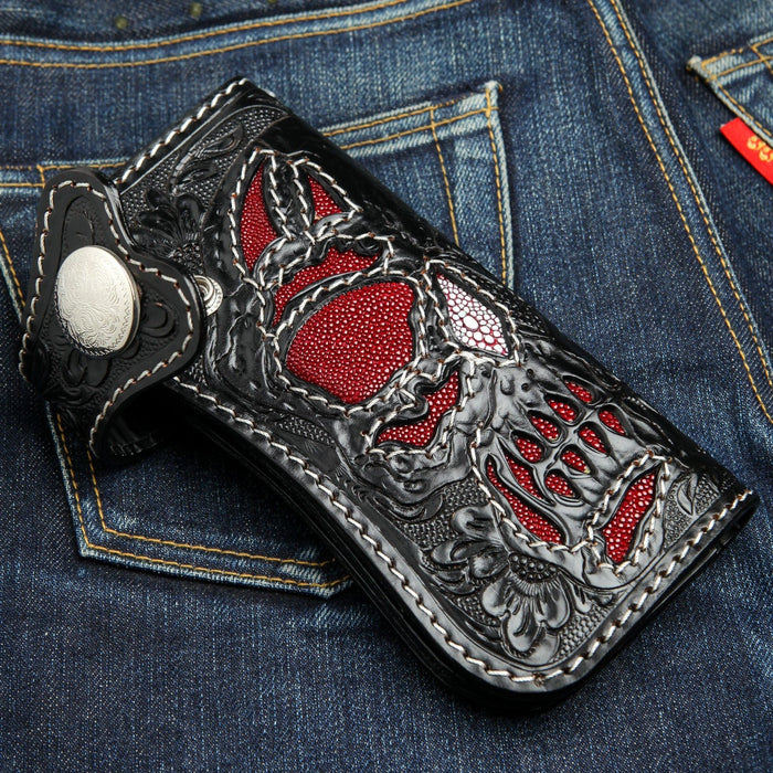 The red and black skull wallet with hand-carved details on a denim background.