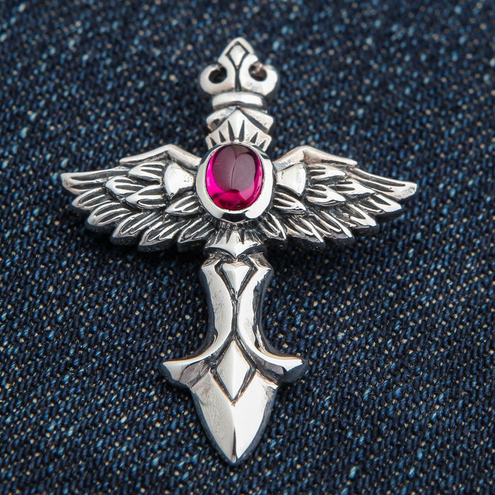 A front view of the sterling silver angel wings cross pendant with a central red cabochon stone, on a denim background.