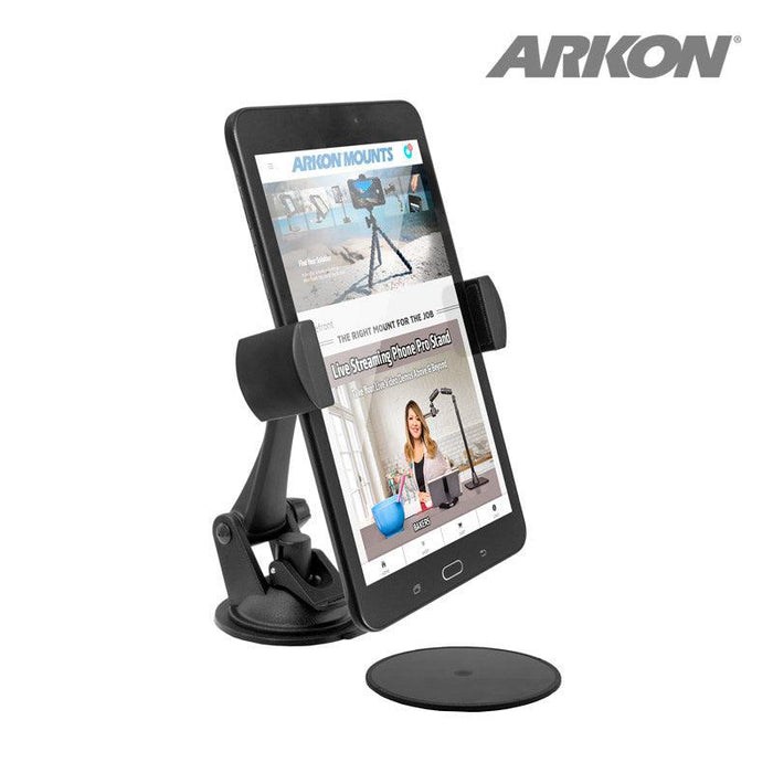 A black RoadVise® XL Car Dash or Windshield Mount holds a smartphone showing a website. The mount features a suction base for surfaces, with the logo in the top right corner and a circular adhesive pad placed in front.