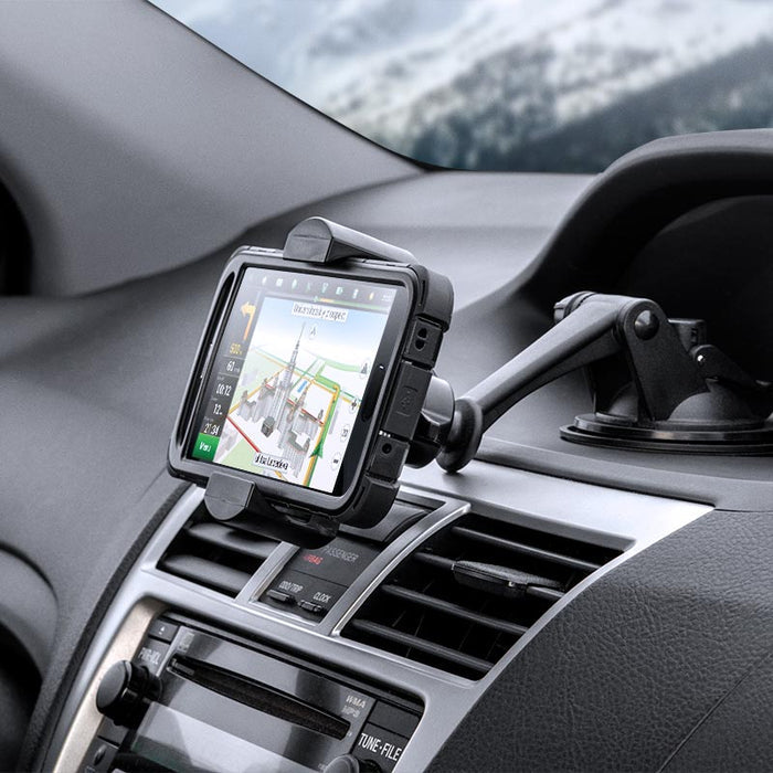 The RoadVise® XL Car Dash or Windshield Mount is attached above the air vents, securely holding a GPS device with navigation directions visible. A blurred winter scene is seen through the windshield.