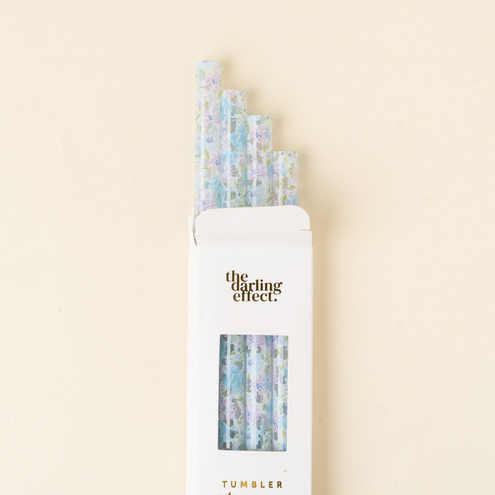 A white box labeled the-darling-effect. Secret Garden Blue 40 oz Tumbler Straw Set holds five BPA-free reusable straws with pastel floral patterns, arranged in a staggered row on a cream-colored background.