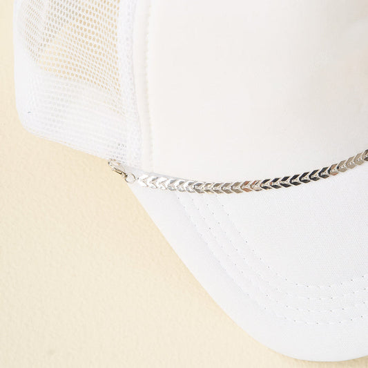 A white mesh trucker hat featuring The Darling Effect's Silver-Leaf Chain Trucker Hat Chain as a bold front-brim accessory, photographed on a light beige background.