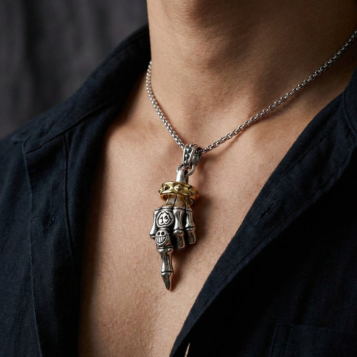 Close-up of a man wearing a sterling silver skeleton hand pendant making the middle finger gesture, featuring a gold studded ring accent and number 13 spade design, hanging on a silver chain against a bare chest.