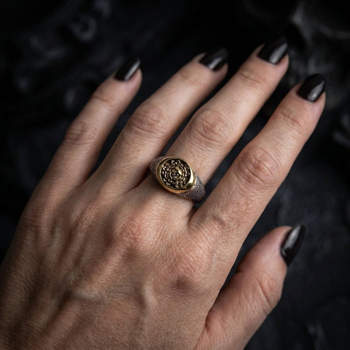 Worn on a woman's hand with black gothic manicure, the gold skull and rose signet ring against a dark moody backdrop