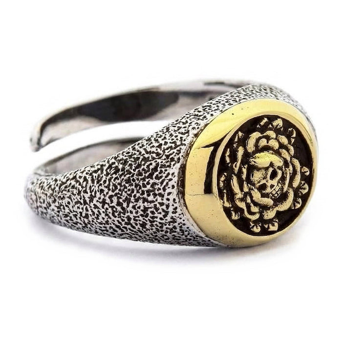 Angled three-quarter view of the silver skull and rose ring showing the domed gold signet and textured shoulders
